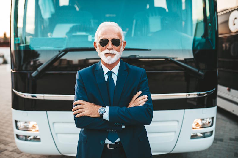 Un conducteur d'autocar aux cheveux blanc et lunettes d'aviateur